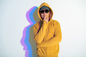 Portrait of calm male standing with multicolored shadow gesturing hand to silence. He looking at camera. Stillness concept