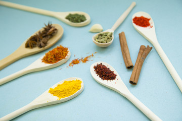 Plastic and glass spoons with dry spices and fresh herbs on a blue background with copy space, top view, close up