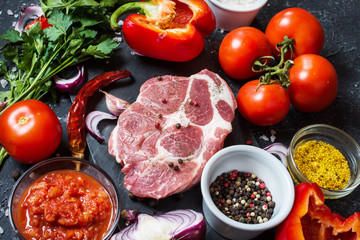 Raw marbled meat steak with ingredients for cooking on dark stone background