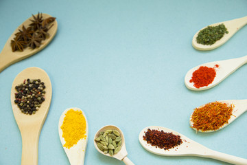 Wooden and plastic spoons with dry spices and fresh herbs on a blue background with copy space, top view, close up
