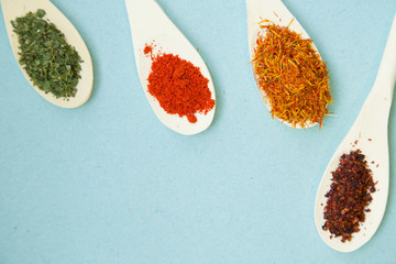 Wooden and plastic spoons with dry spices and fresh herbs on a blue background with copy space, top view, close up