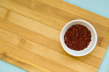 Plastic cup with dry spices and fresh herbs on a wooden cutting board with blue background, top view, close up