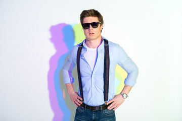 Portrait of assertive male in sunglasses with hands on hips. He has multicolored shadow. Assuredness concept