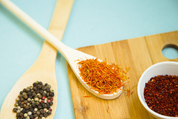 Wooden spoon with dry spices and fresh herbs on a wooden cutting board with blue background, top view, close up