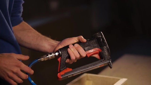 Professional carpenter is connecting air tube to the staple gun. Getting ready to use the tool.