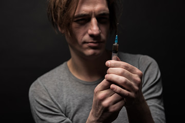 Portrait of serious male filling hype with narcotic substance with concentrated face. Focus on syringe. Isolated on background