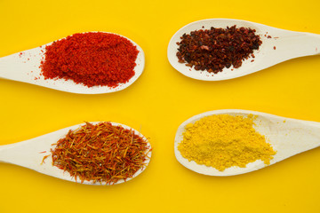 Wooden and plastic spoons with dry spices and fresh herbs on a yellow background with copy space, top view, close up