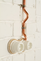 A vintage outlet and electrical wiring in a copper tube.