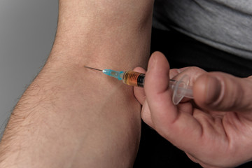 Close up of injector with narcotic stubbing male hand. Bad habit concept