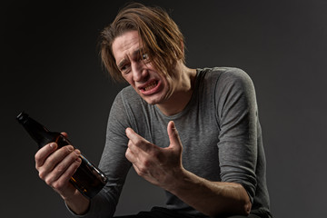 Waist up portrait of man with alcohol dependence looking at bottle with perplexity. Isolated on...