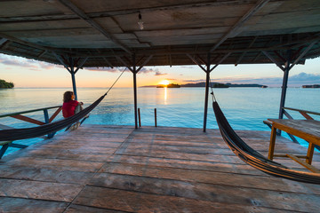 Togean Islands Sunrise, Togian Islands travel destination, Sulawesi, Indonesia. Woman looking at view on hammock, transparent turquoise water with scattered islets.