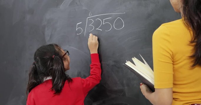 Asian student working on a math question on blackboard with her teacher standing next to her