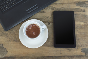 Laptop, tablet and coffee cup on old wooden table.