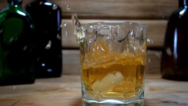 Slow motion of falling a piece of ice into a glass of whiskey on a wooden background.