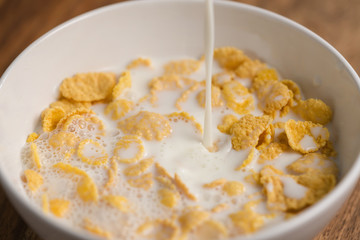 pouring milk into corn flakes in white bowl closeup
