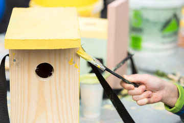 artist job, drawing, repairing concept. close up of nesting box that is not prepared for using yet, in the soft arm there is a brush for painting this wooden box in sunny yellow color