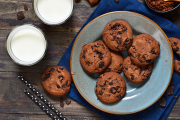 Homemade chocolate cookies in a plate with milk on a wood background.