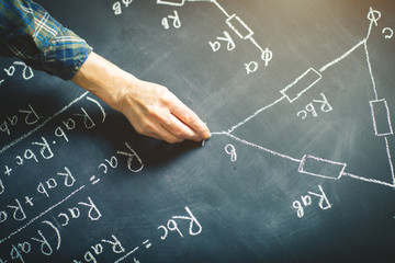 The teacher writes on a board with chalk a formula for electric current.