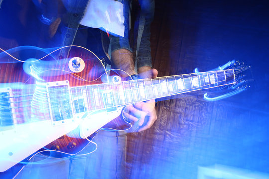 performance, creativity, rock style concept. close up of guitar in the arms of caucasian male musician, that figure is getting lost and blurred on the dark background