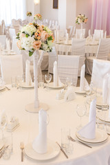 floral arrangement, interior, celebration concept. there is adorable table of restaurant served with white plates and tall and elegant glasses, in the center of table there is a bouquet of flowers