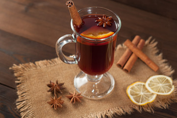 Red mulled wine on burlap on a wooden table with various spices