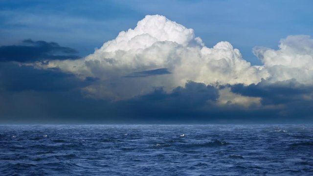 Dark blue restless sea, waves with white foam, towering cumulus clouds on horizon