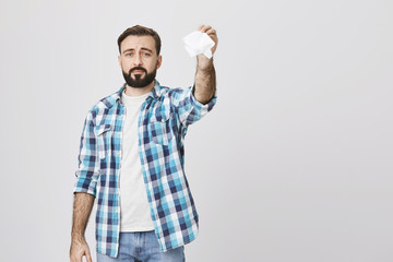 Indoor shot of gloomy sad bearded adult man holding tissue in hand and waving it like saying goodbye, standing over gray background. Father send off daughter to summer camp for the first time.