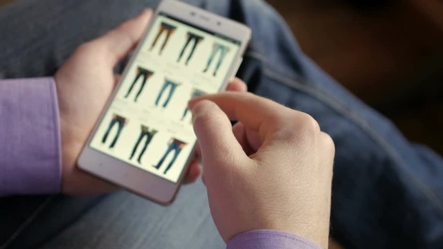 A man looks at the goods in the online clothing store. People using Smartphone, online shopping.  The screen is blurred.  Close-up. 4K UHD.