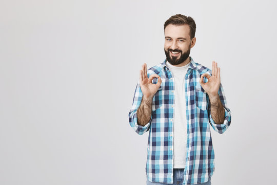 Portrait Of Happy Handsome Bearded Male Saying Everything Is Okay And Fine With Gesture, Standing Over Gray Background. Hey, I Got It, Everything Will Be Done Perfectly