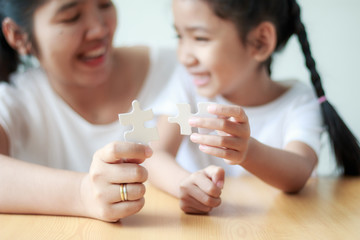 Asian little girl playing jigsaw puzzle with her mother for family concept shallow depth of field select focus on hands