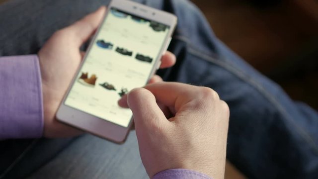 A man looks at the goods in the online shoes store. People using Smartphone, online shopping. The screen is blurred. Close-up. 4K UHD.