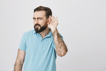 Handsome man with a beard looking confused standing with hand near his ear trying to hear something. It is very loud on a concert so person tries to understand what his friend is saying
