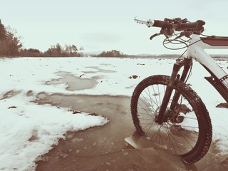 Bike drowned in muddy pool within winter trip. Broken pieces of ice around freeze terain tyre