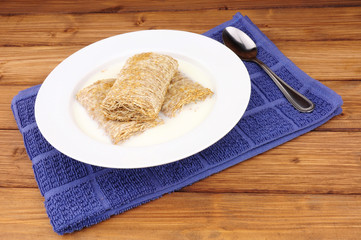 Bowl of shredded wheat breakfast cereal with milk on a wood background