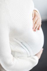 future, pregnancy, motherhood concept. there is close up of young womans hands on her belly covered with knitted sweater, she is pregnant that is why she is tenderly hugging her belly