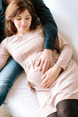 love, feelings, birth giving concept. there is extremelly beautiful expecting woman dressed in lovely dress of powdery colour, arm of her husband is tenderly huggin her