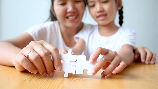 4K Asian little girl playing jigsaw puzzle with mother select focus on hand shallow depth of field