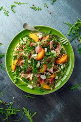 Fresh Peach salad with Parma ham, feta cheese and vegetables in a green plate. healthy food