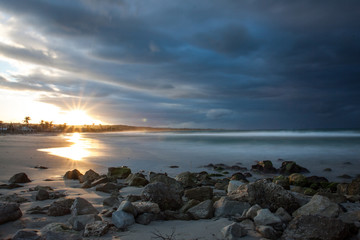 Fototapeta na wymiar Sonnenuntergang am Strand mit Steinen, Palmen und dunklen Wolken in Kuba