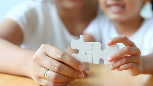 4K Asian little girl playing jigsaw puzzle with mother select focus on hand shallow depth of field