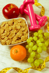 Diet fitness concept - dumbbells, measuring tape, flakes and fresh fruits on wooden table.