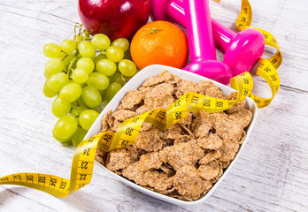 Diet fitness concept - dumbbells, measuring tape, flakes and fresh fruits on wooden table.