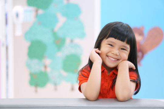 Asian children cute or kid girl happy fun and smile with wear red shirt on sofa at preschool or nursery and child hospital with space