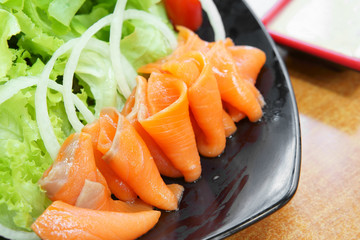 delicious salmon roll with vegetable salad and salad dressing in black dish on wood table for healthy food and diet at lunch or dinner in japanese food restaurant with space