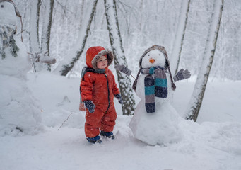 European boy and the snowman in a snowy forest