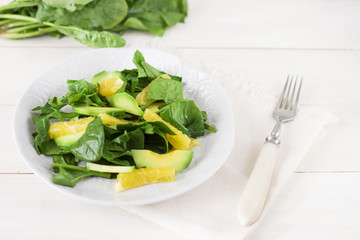 Raw salad of spinach, avocado and orange on a white wooden background