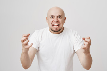 Angry and insane bald bearded guy expressing his readiness to kill somebody, being filled with anger and negative emotions, standing over gray background and gesturing. Employer is mad
