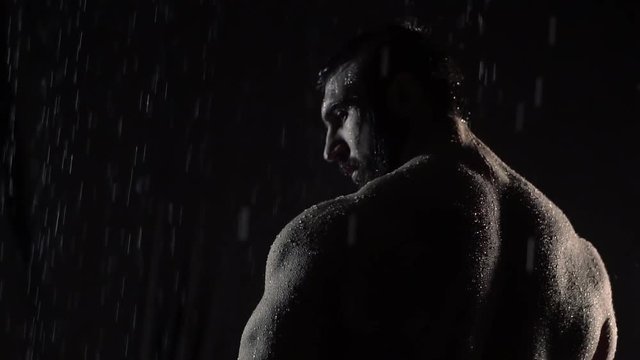 a sporty man stands in the rain, drops fall on his bare back, he looks back