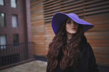 Beautiful charming young woman with long hair in a ultraviolet color hat is on the background of wooden wall. Luxurious brown hair waving from the wind. The tear on her cheek. 