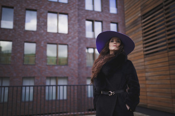 Beautiful charming young woman with long hair in a ultraviolet color hat is on the background of wooden wall. Luxurious brown hair waving from the wind. The tear on her cheek. 